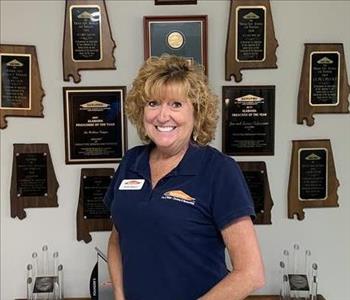 Photo of female employee smiling in front of wall with awards hanging